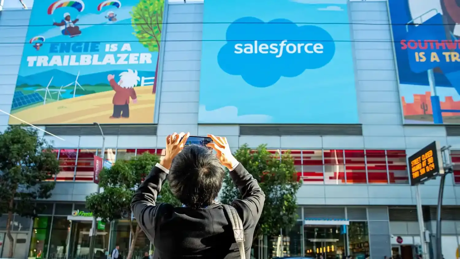 Someone taking a photo outside of a Salesforce office building. A bunch of illustrated mascots are on a billboard reading "Engie is a Trailblazer"